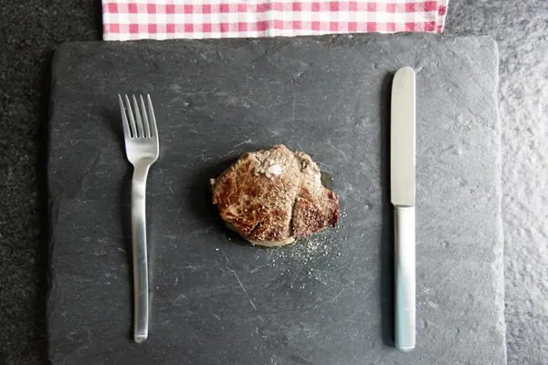 Seared sirloin steak on a slate board between a fork and knife
